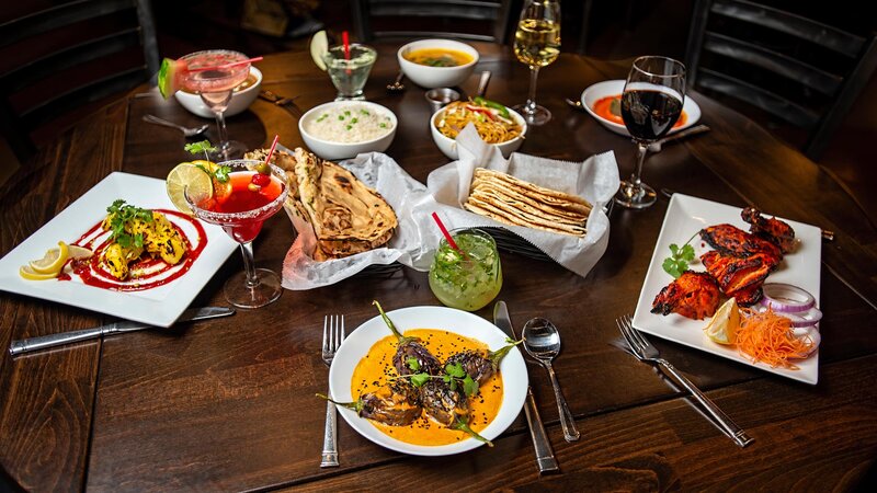 Dining room table with many entrees, appetizers, naan bread and cocktails